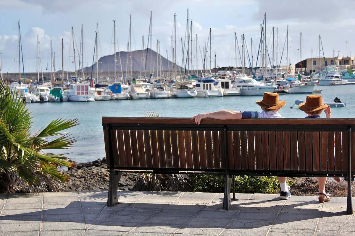 Retired couple sitting on a bench overlooking a marina with boats, symbolizing a peaceful lifestyle associated with a Thailand retirement visa.